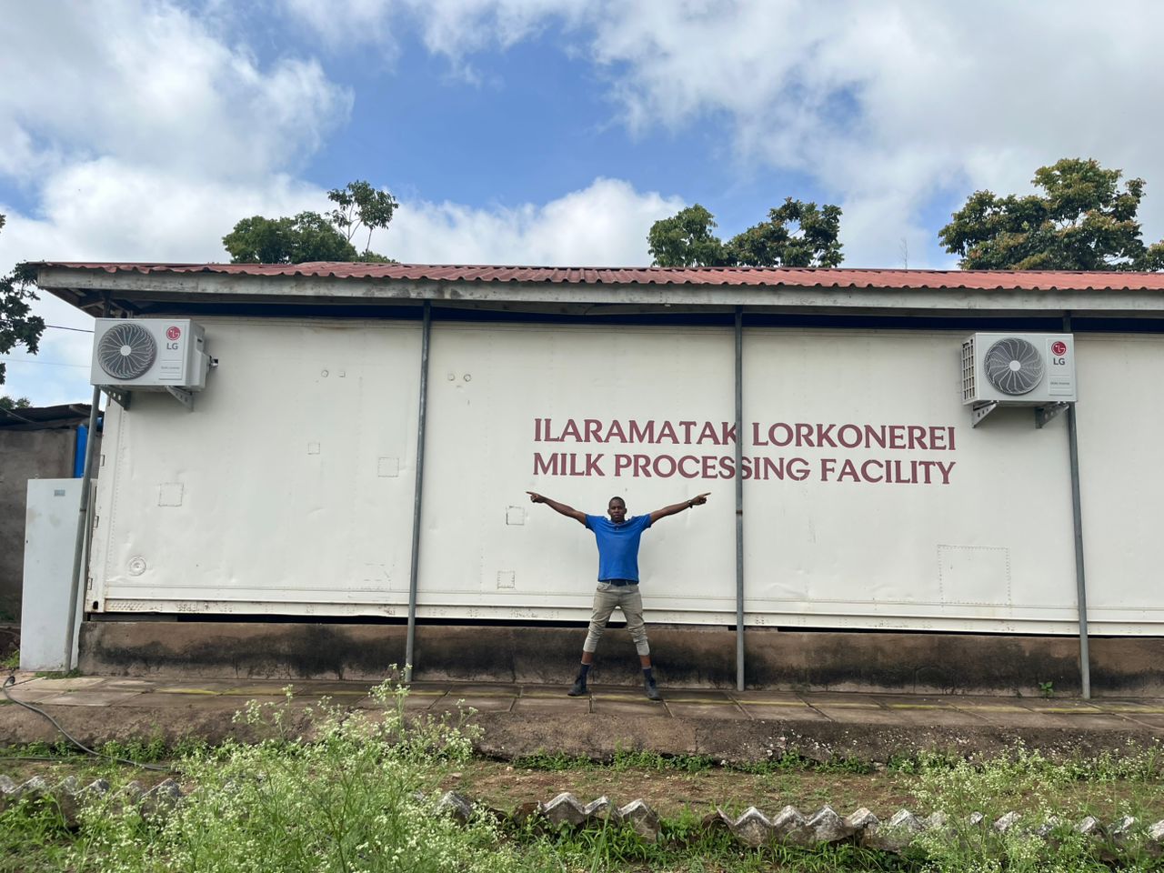 A person stands with arms raised in front of the dairy processing plant.